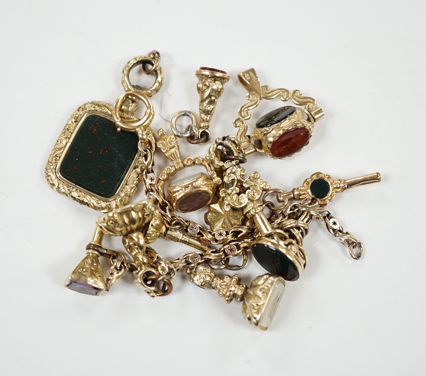 An early 20th century yellow metal charm bracelet (a.f.), hung with five assorted watch keys, together with seven assorted yellow metal overlaid and chalcedony set fobs.